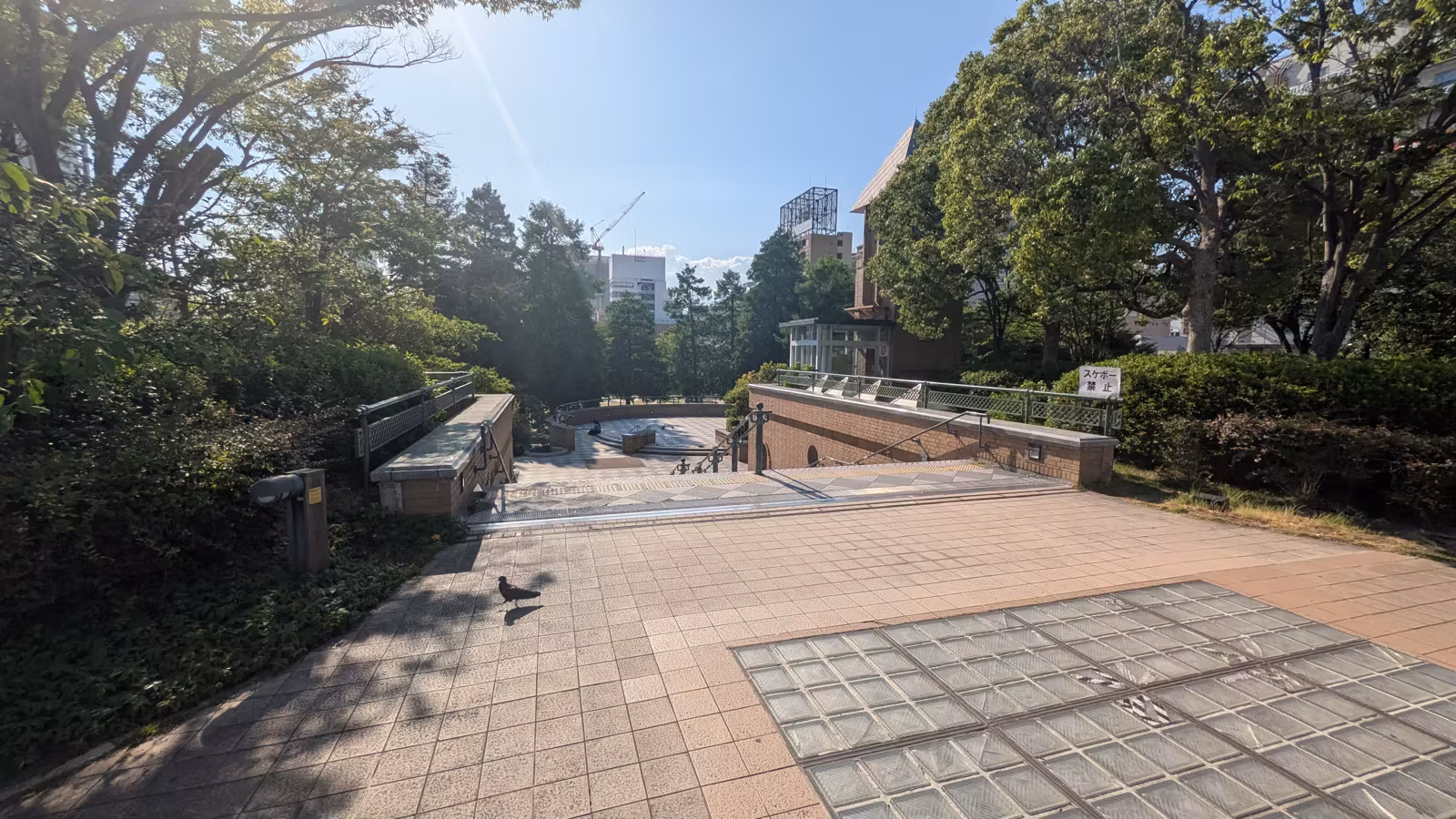中央公園の石畳の広場。木々に囲まれ、奥に階段とテラスが見える