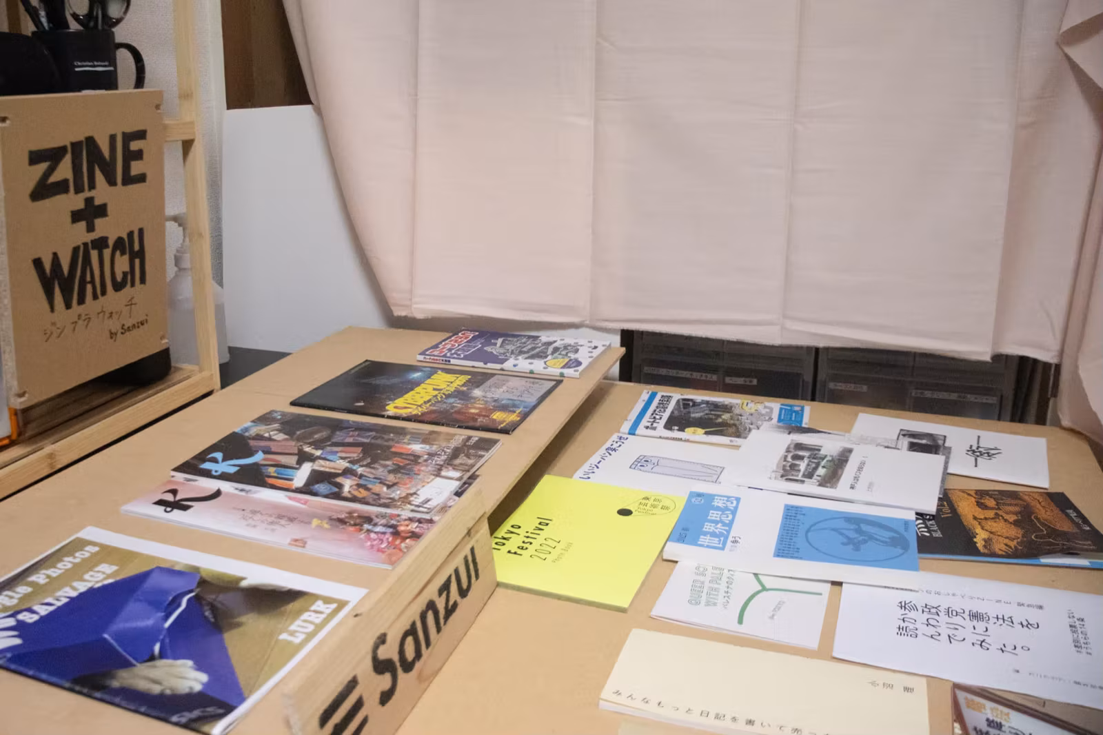 「ZINE + WATCH」の看板と机に広げられたZINEの数々