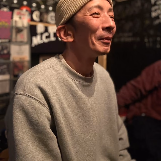 ニット帽にグレーのスウェットで、店内で笑う TA2Soul