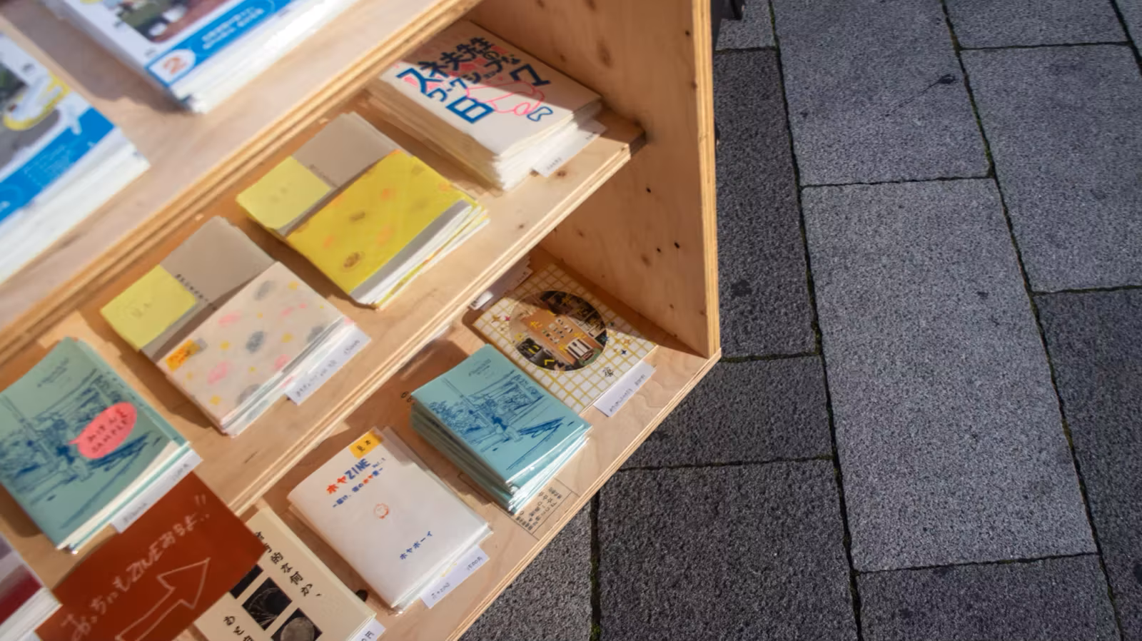 屋外の木製の棚に並んだ小さなZINEや冊子
